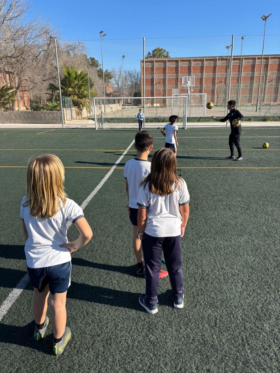 Grupo de alumnos con balones alrededor del entrenador